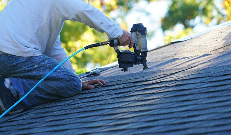 A homeowner examines damaged asphalt shingles and granules missing on a residential house roof.