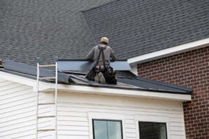 A person using a roof rake to remove snow from a house roof on a cold, clear day.